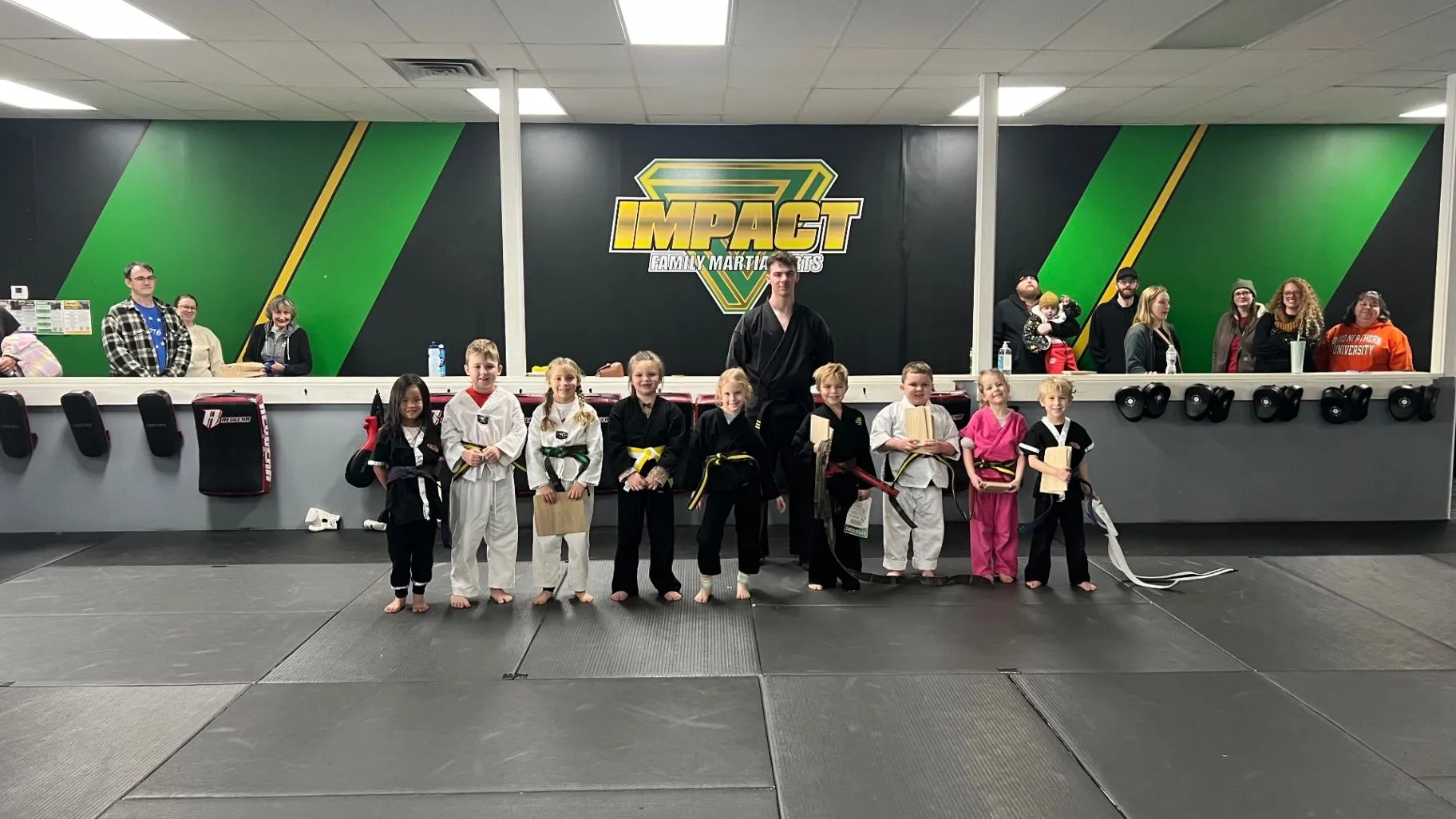 Young martial arts students and families gathered inside the Impact dojo